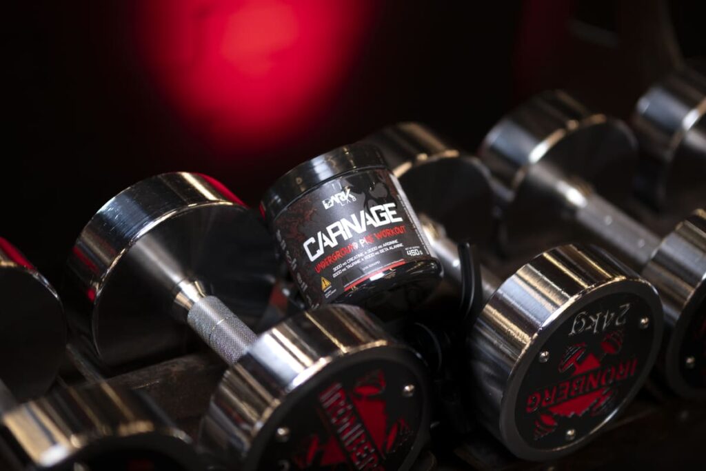 Pote do pré-treino Carnage (DARK LAB) sobre halteres de 24kg. Representa suplementação para maximizar a performance em treino full body.