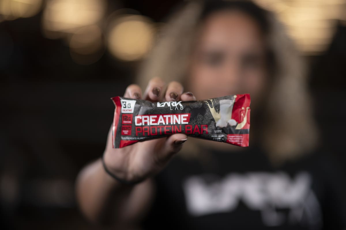 Mulher exibe uma barra de proteína com creatina da Dark Lab, mostrando como snacks práticos e nutritivos podem fazer parte de uma dieta flexível.