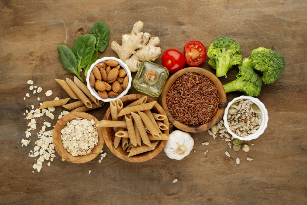 Várias tigelas de comida com massas, sementes, vegetais e nozes dispostas em uma tábua de madeira. A imagem representa como incluir fibras alimentares no dia a dia.