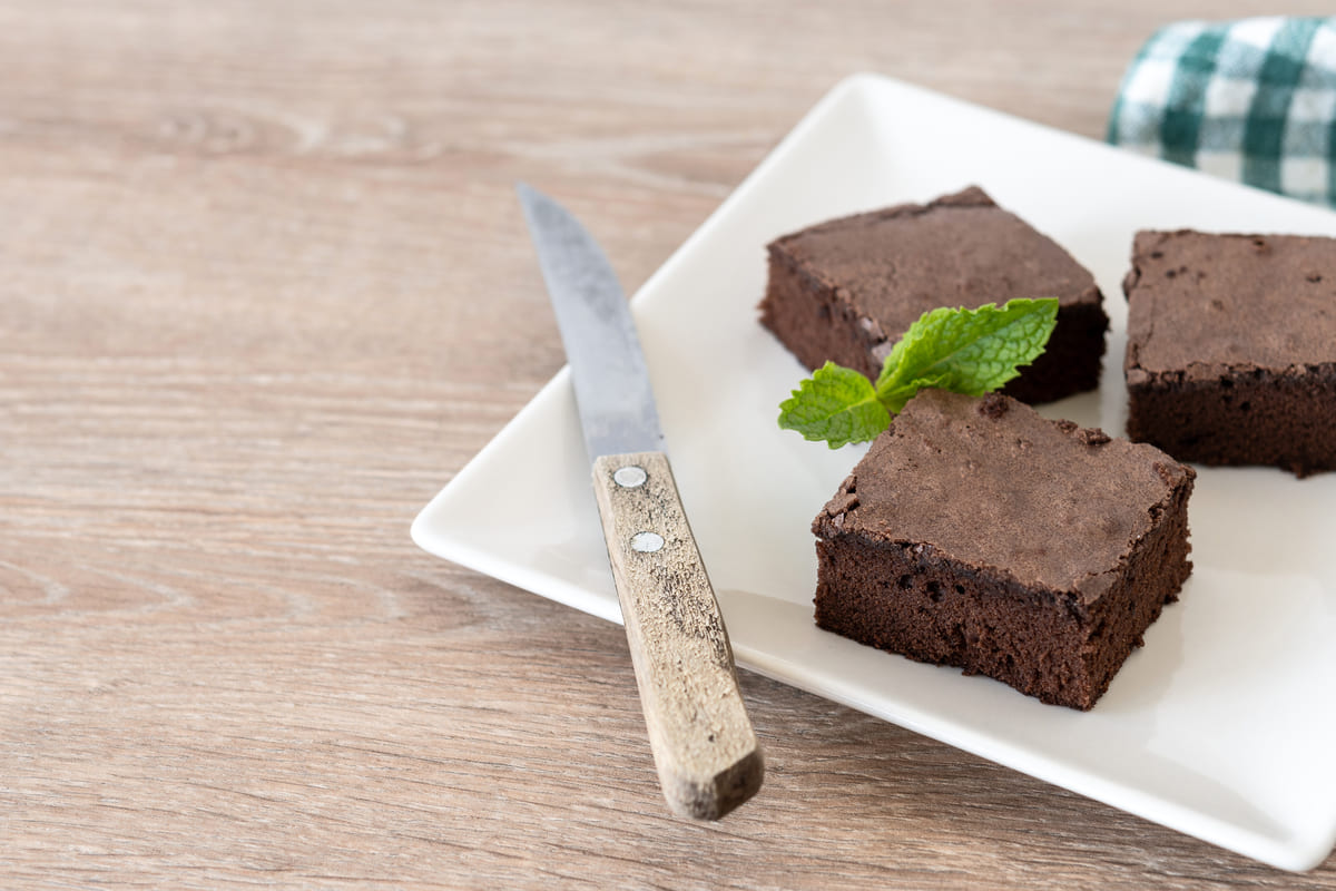 Pedaços de brownie de chocolate em um prato branco, uma das receitas de sobremesas fit, decorados com uma folha de hortelã.