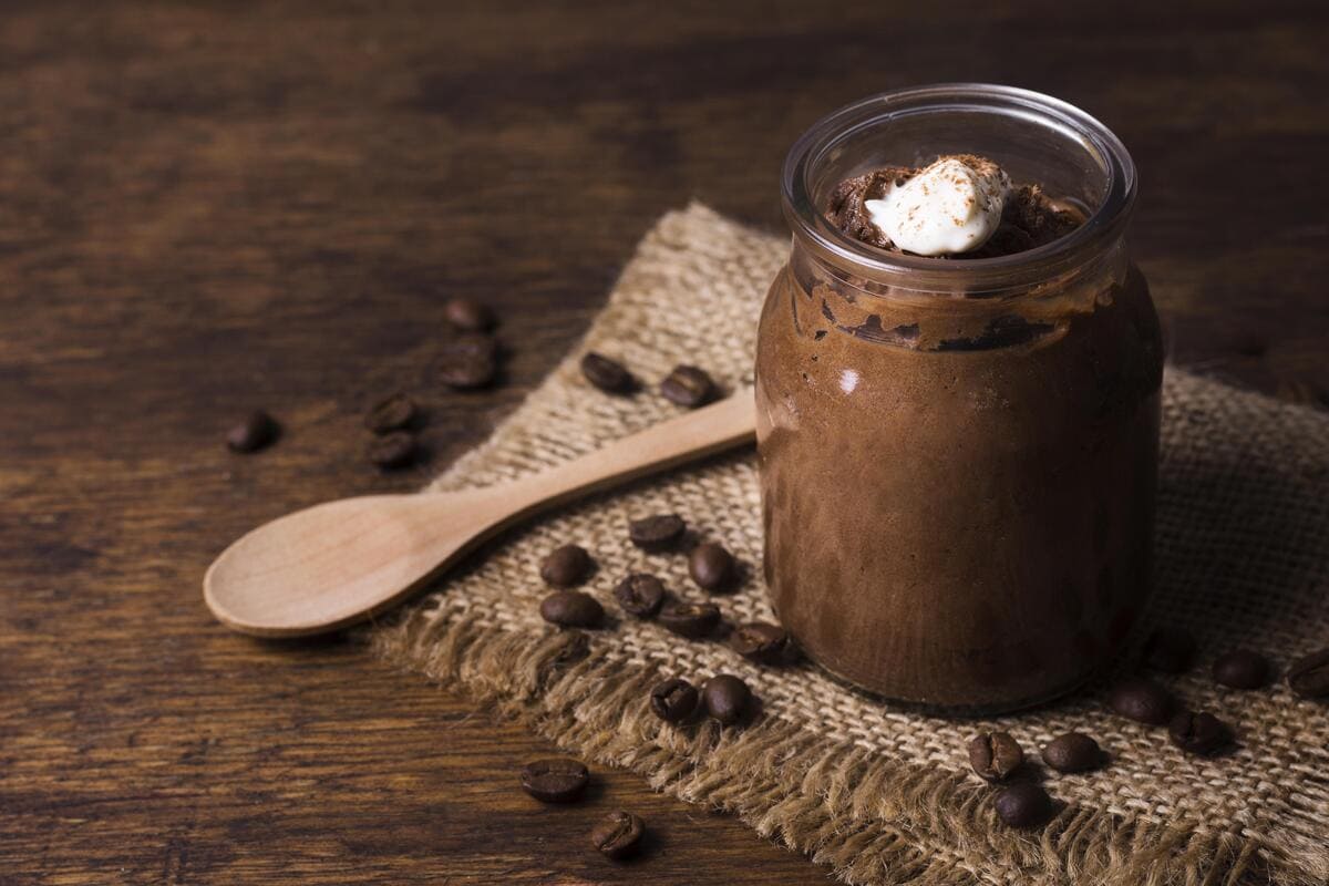 Mousse de chocolate servido em um pote de vidro, uma opção de sobremesas fit, sobre um tecido de juta com grãos de café.