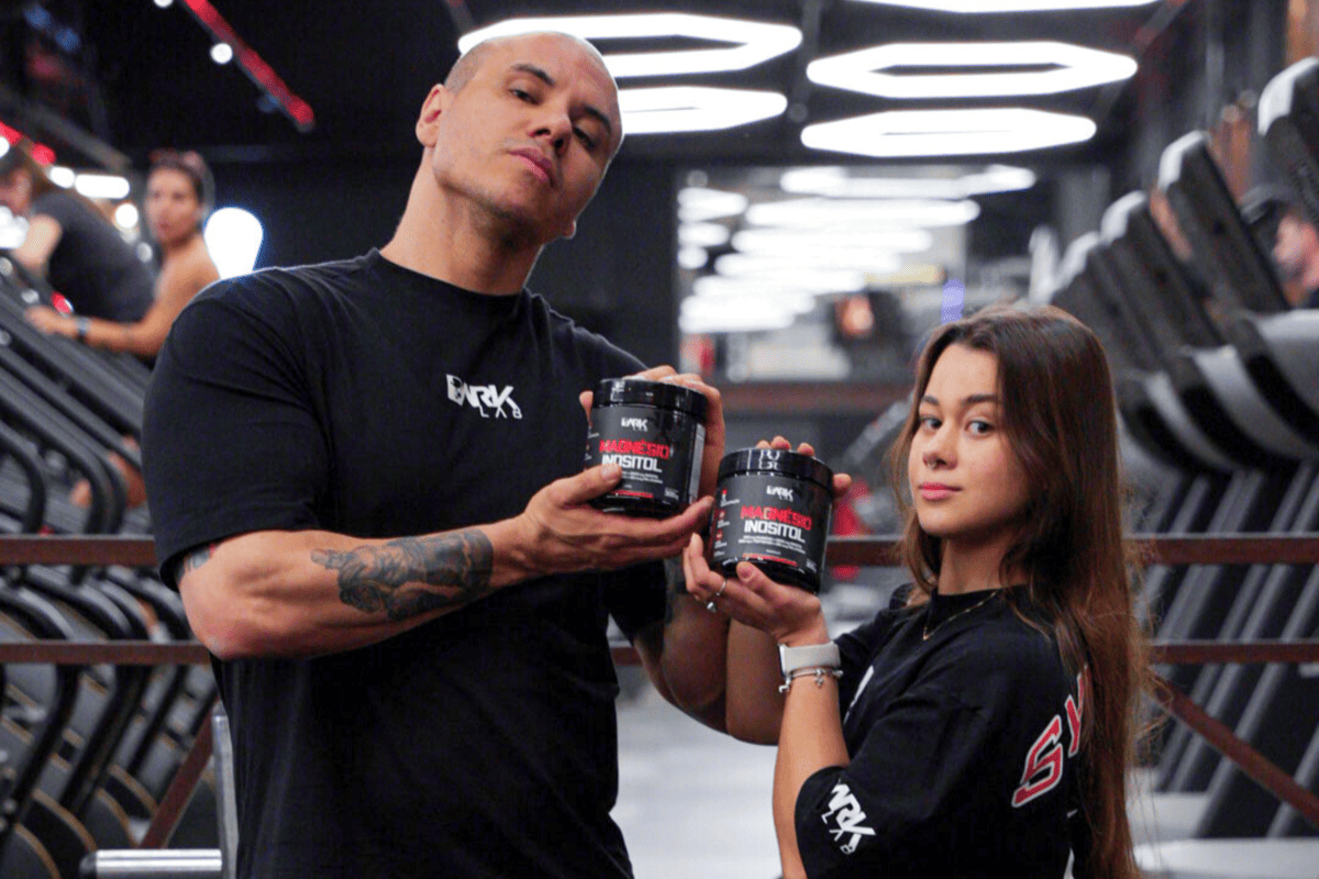 Homem e mulher em academia segurando potes de suplemento DARK LAB "Magnésio Inositol", que está em oferta na Black Friday 2025.