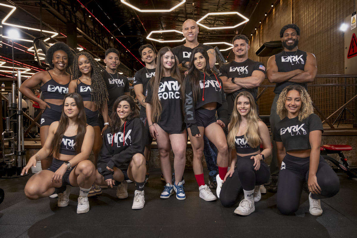 Equipe DARK LAB, composta por atletas diversos (homens e mulheres), posa em uma academia, prontos para a Black Friday do mercado de suplementos.