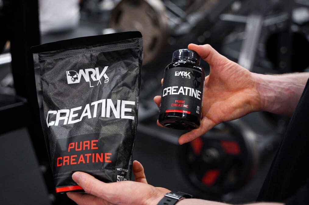 Mãos apresentam embalagens em saco e pote da Dark Lab Pure Creatine na academia, ilustrando opções de creatinas aprovadas pela anvisa.