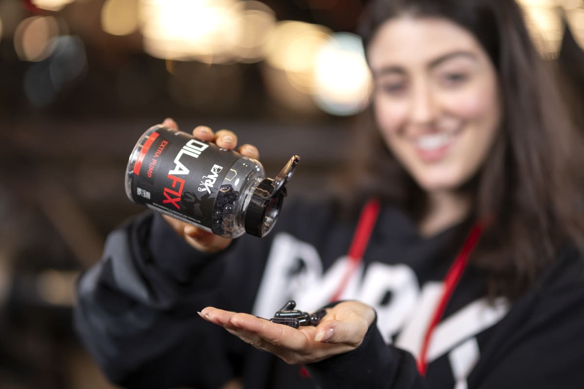 Mulher sorrindo, segurando um frasco de suplemento Dilafix Dark Lab, despejando cápsulas na mão, simbolizando a qualidade e a variedade que você encontra na melhor loja de suplementos online.