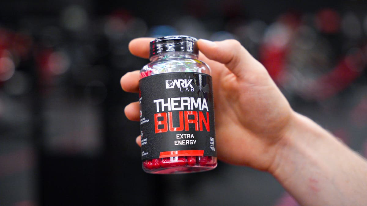 Mão segura frasco transparente contendo cápsulas vermelhas do termogênico Therma Burn, uma opção de energia entre os suplementos para mulheres.