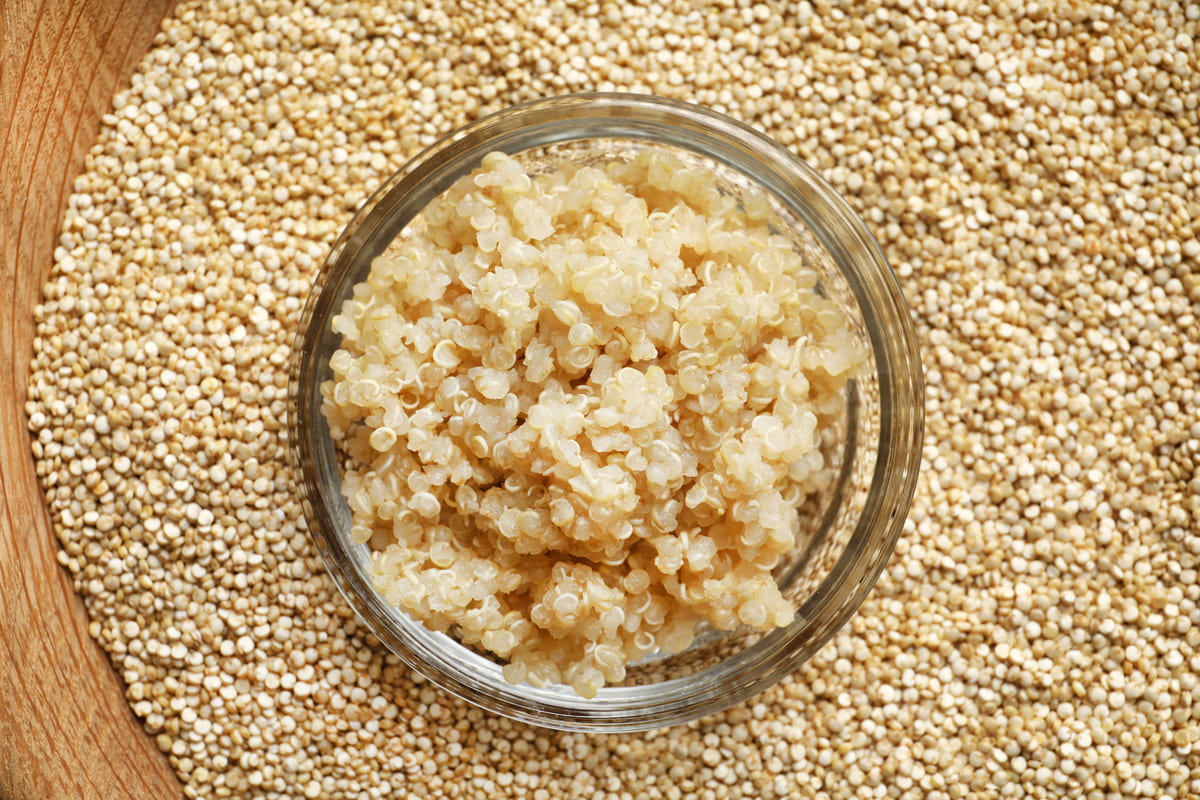 Vista superior de quinoa, um dos alimentos ricos em carboidratos, cozida em uma tigela de vidro, centralizada sobre quinoa crua.