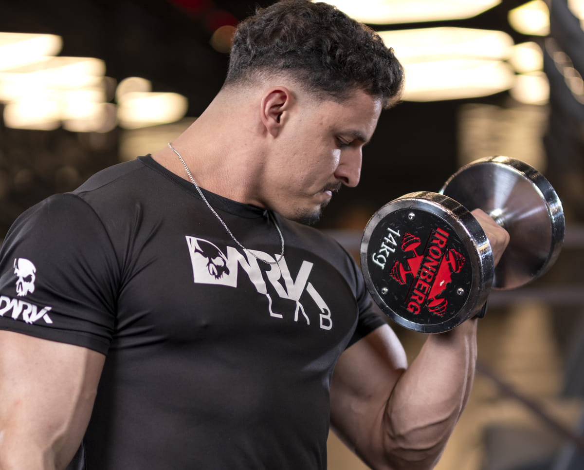 Atleta da Dark Lab realiza exercício com halter na academia. O levantamento de peso é parte fundamental de uma rotina de powerlifting focada em ganho de massa muscular.