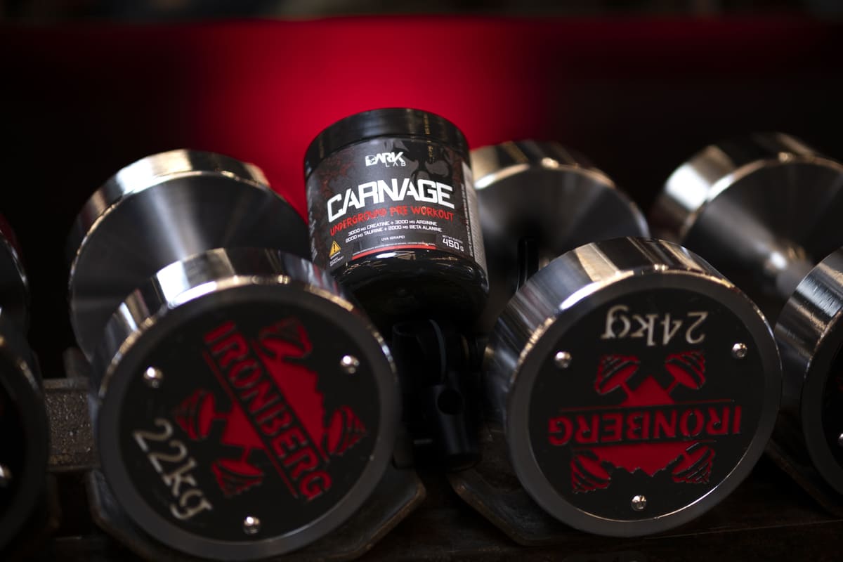 Pré-treino Carnage da Dark Lab entre halteres na academia, integrando a rotina fitness para mais foco e intensidade nos treinos.